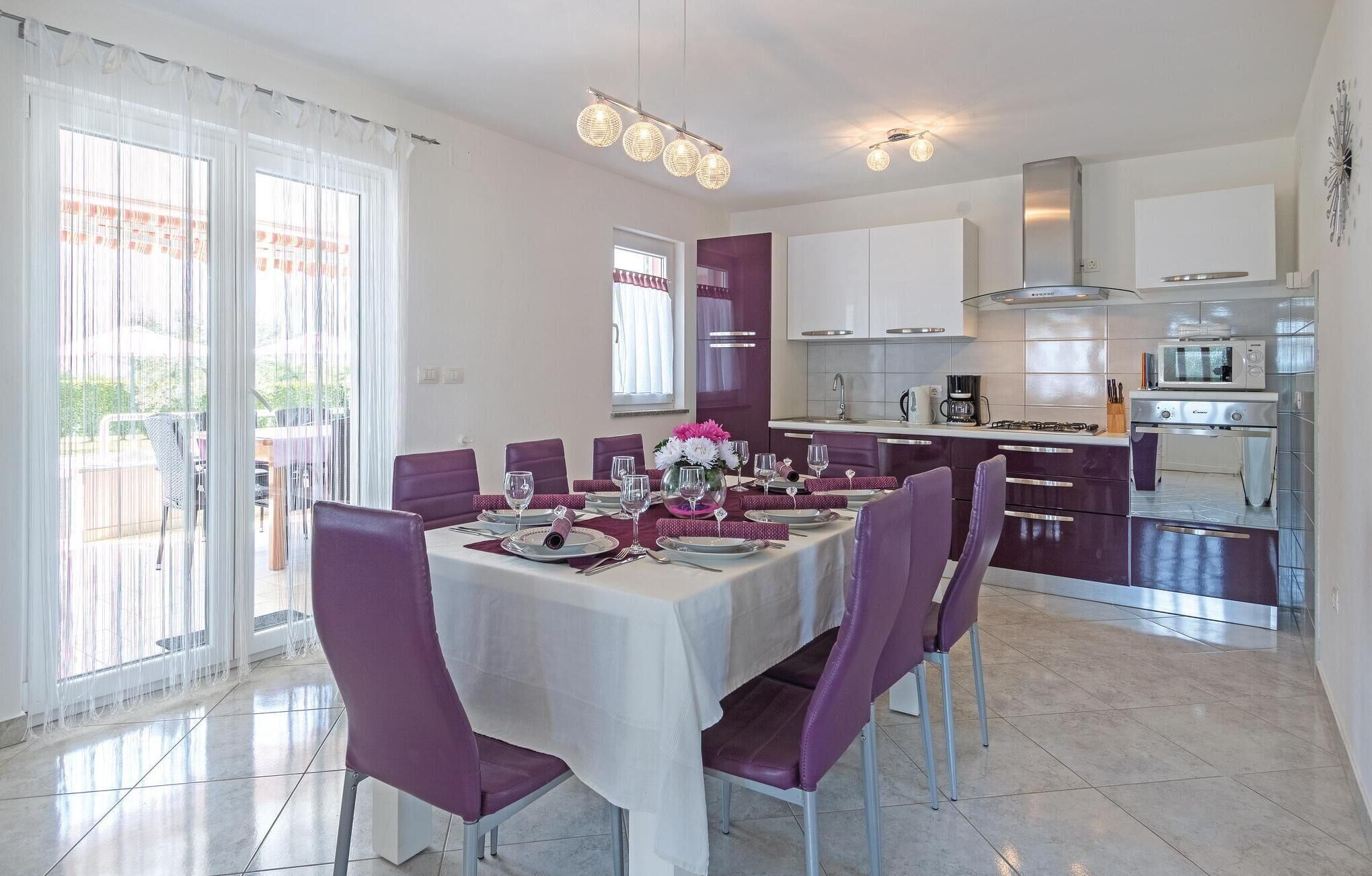 A dining area with a table set for six, purple chairs, and a kitchen in the background.