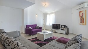 Una sala de estar moderna con un sofá, un sillón morado, una mesa de centro, un televisor y un cuadro en la pared.