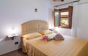 Un dormitorio con una cama grande, una mesita de noche con lámpara, una ventana con cortinas y un pequeño adorno en la pared.
