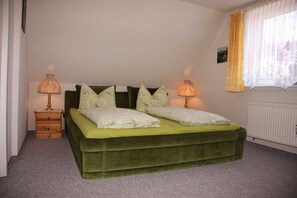 Une chambre avec un lit vert, deux tables de chevet avec des lampes, une fenêtre avec un rideau et un radiateur.