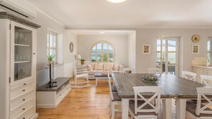 Un comedor amplio con una larga mesa de madera, sillas blancas y vistas al exterior a través de un gran ventanal arqueado.