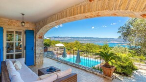 Un balcón con arco de piedra, piscina y vistas al mar y a las montañas.