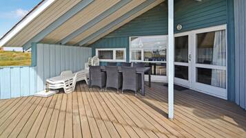 Un espace extérieur abrité doté d’une terrasse en bois, d’une table avec des chaises et d’une fenêtre avec des rideaux.