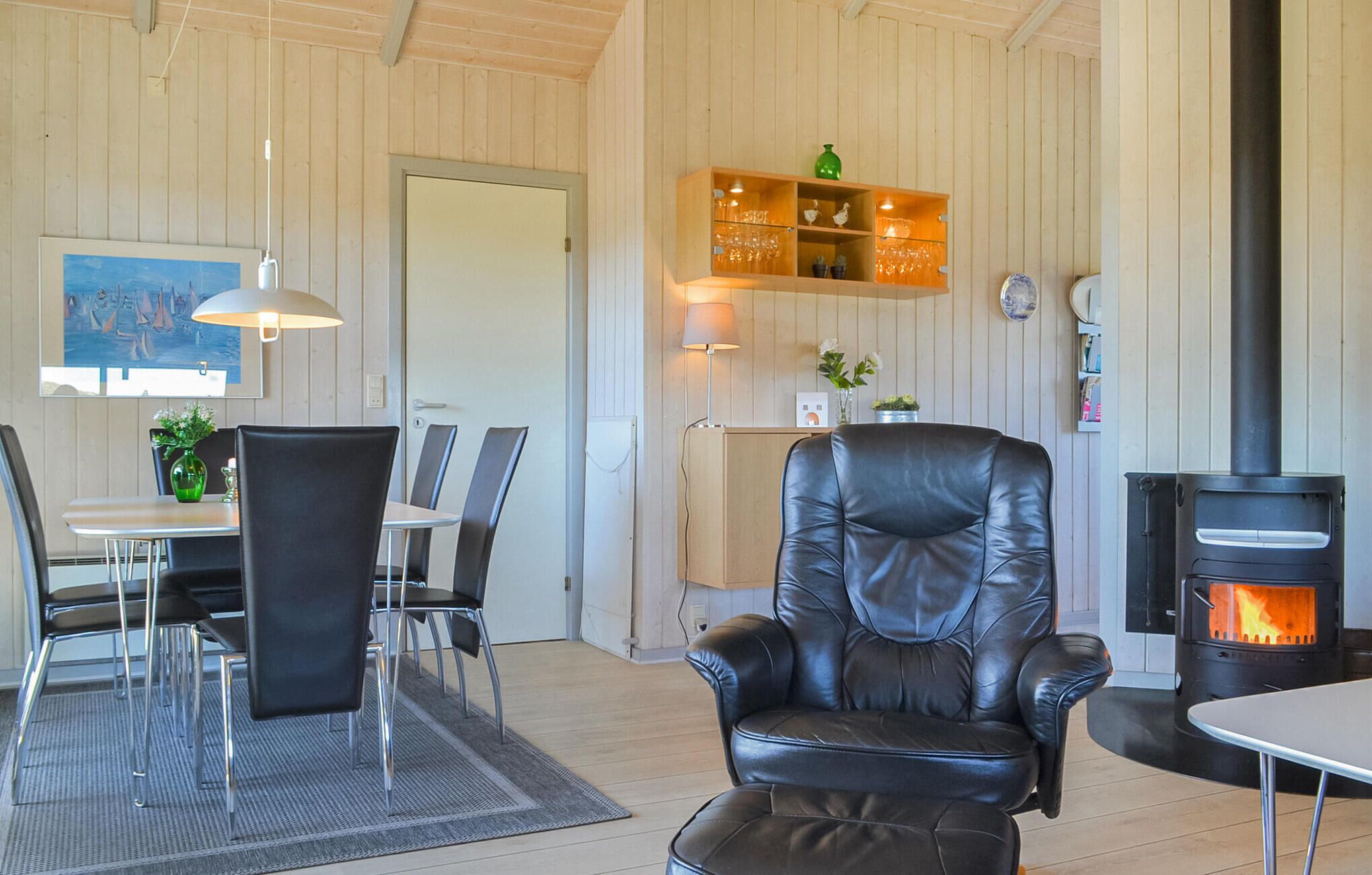 Une pièce chaleureuse avec un fauteuil en cuir, une table à manger avec des chaises, un meuble en bois avec des étagères, une cheminée et un tableau accroché au mur.