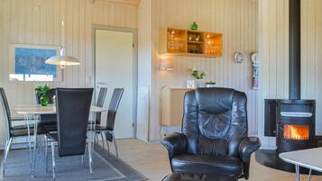Une pièce chaleureuse avec un fauteuil en cuir, une table à manger avec des chaises, un meuble en bois avec des étagères, une cheminée et un tableau accroché au mur.