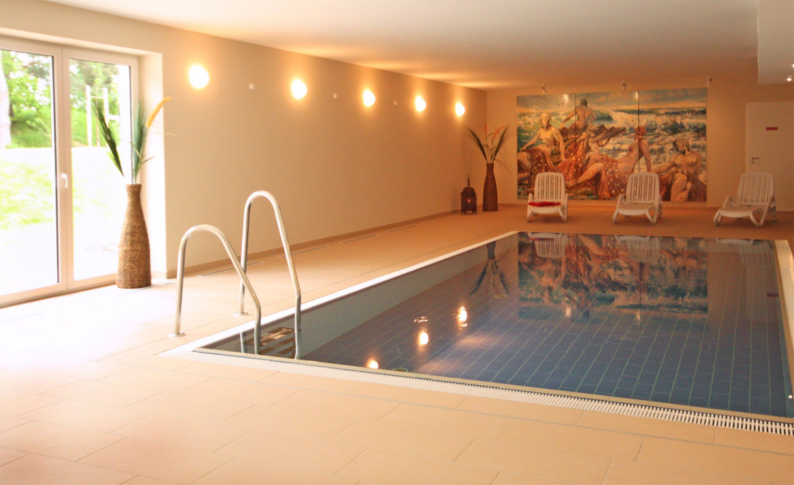 Une piscine intérieure offrant une vue dégagée sur l’eau, un ensemble de chaises blanches et un grand tableau accroché au mur.