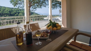 A table set with bottles, glasses, and a bowl of fruit on a balcony with a view of a forested landscape. - 3 bedroom gorgeous home in Duba (Duba)