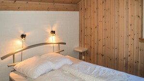 A bed with white bedding, a wooden headboard, and two wall-mounted light fixtures. - Cozy home in ålbæk with sauna (Ålbæk)