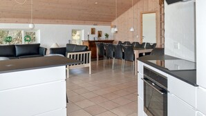 A modern kitchen with a dining area, featuring a wooden ceiling, white cabinetry, and a built-in oven. - Cozy home in ålbæk with sauna (Ålbæk)
