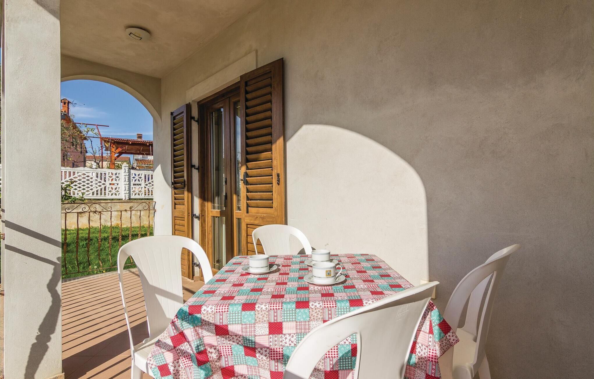 A balcony with a table set for two, white chairs, and a tablecloth.
