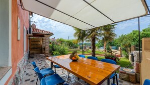 Eine Terrasse im Freien mit einem Holztisch und blauen Stühlen, umgeben von einer weißen Markise.
