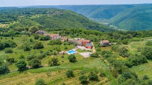 Ländliche Landschaft mit einer Häusergruppe, umgeben von üppigem Grün und sanften Hügeln.