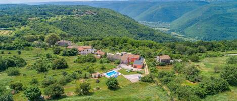 A rural landscape with a cluster of houses surrounded by lush greenery and rolling hills.