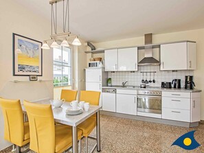 Une cuisine moderne avec des meubles blancs, une cuisinière en acier inoxydable et un coin repas avec des chaises jaunes et une table dressée pour quatre personnes.