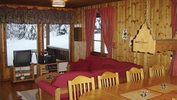 Interior acogedor de una cabaña con una mesa de comedor de madera, un sofá tapizado en rojo y un televisor en una esquina.