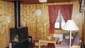 Una cabaña acogedora con estufa de leña, un sofá, una mesa y un ventanal con cortinas.
