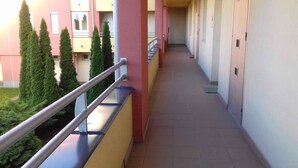 Un couloir avec une rambarde en métal, un sol carrelé et une rangée de portes d’un côté.
