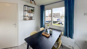 Un'area pranzo con un tavolo nero, due sedie, un piccolo ripiano con oggetti decorativi e una finestra vista barche.