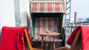 Ein Balkon mit zwei Holzstühlen, einem kleinen Tisch und einer karierten Bank.