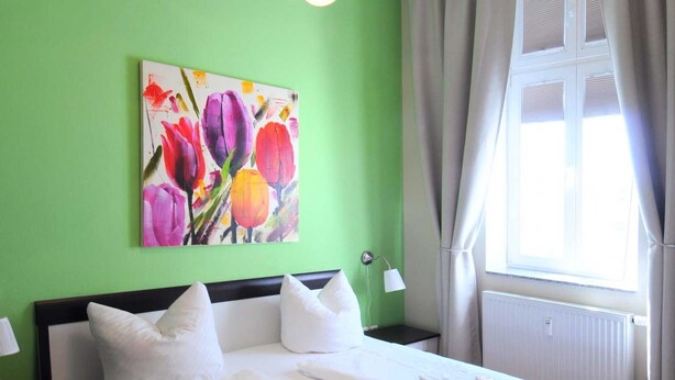 Ein Doppelbett mit weißen Bettwäsche, eine grüne Wand, ein Blumenbild und ein Fenster mit Vorhängen.