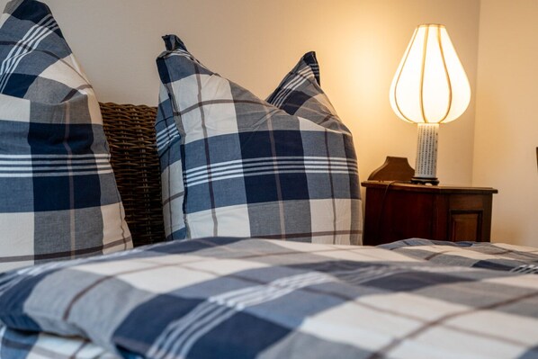 A bed with a checkered bedspread and pillows, a wicker basket, and a bedside table with a lamp.