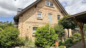 A two-story brick house with a gabled roof, a front porch, and a garden with various plants and a brick pathway.