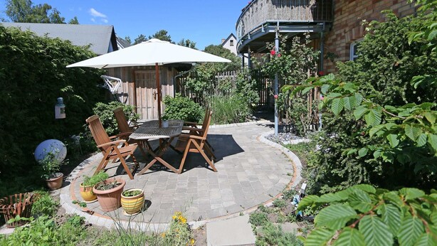 A patio with a table and chairs, surrounded by potted plants and a brick wall.