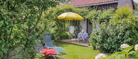 A garden with a red-roofed building, a yellow umbrella, and outdoor furniture.