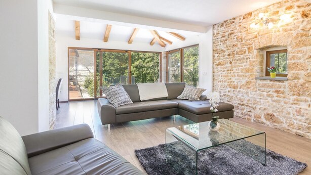 A modern living room with a sectional sofa, a glass coffee table, and a stone wall. - Stunning home in Sv.Petar u Sumi (Sv.Petar u Sumi)
