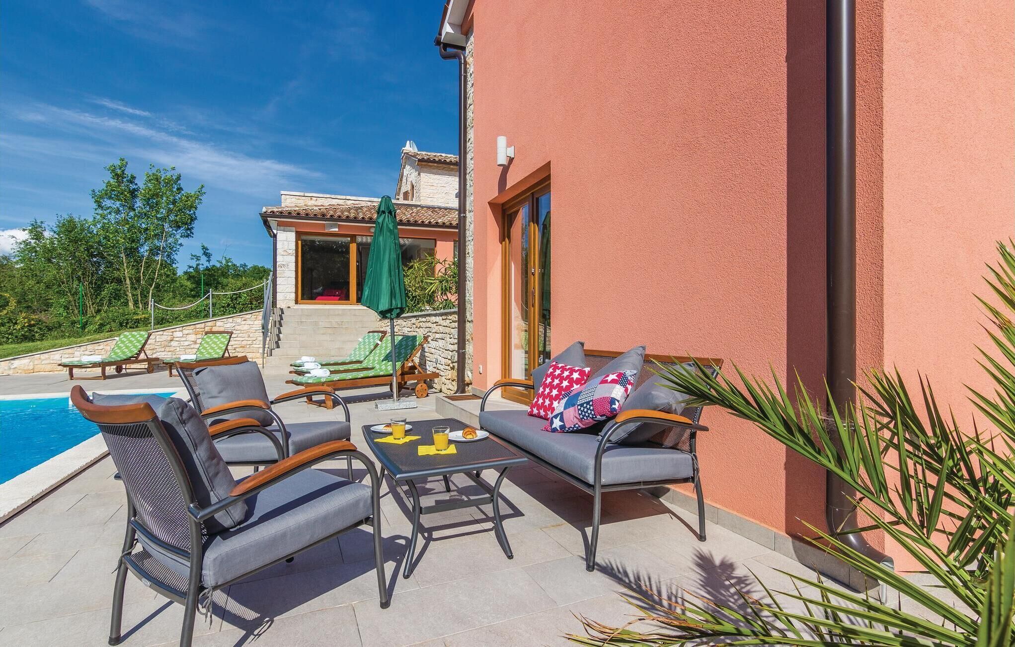 A poolside area with lounge chairs, a table with a drink, and a view of a building with a stone facade.
