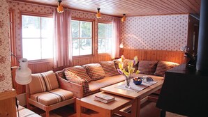 A cozy room with a sofa, a table, and a piano. There are windows with curtains and a lamp on the wall. - Pet friendly home in Oviken with sauna (Oviken)