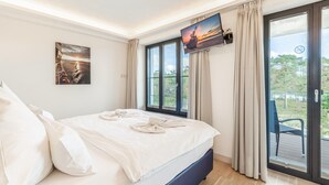 A bedroom with a bed, a TV mounted on the wall, and a large window with curtains.
