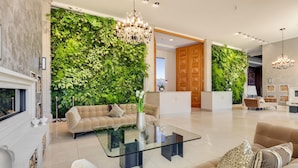 Una sala de estar moderna con una mesa de centro de vidrio, sofás color beige, una chimenea y una pared verde con plantas.