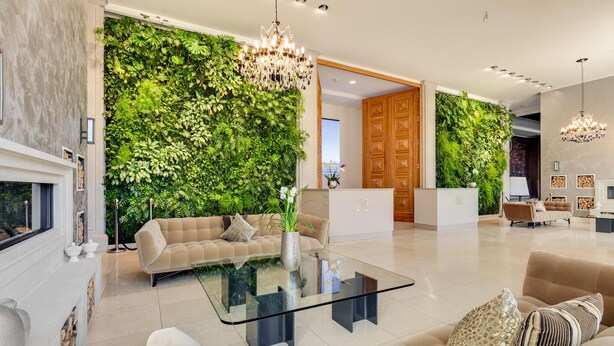 A modern living room with a glass coffee table, beige sofas, a fireplace, and a green wall with plants.