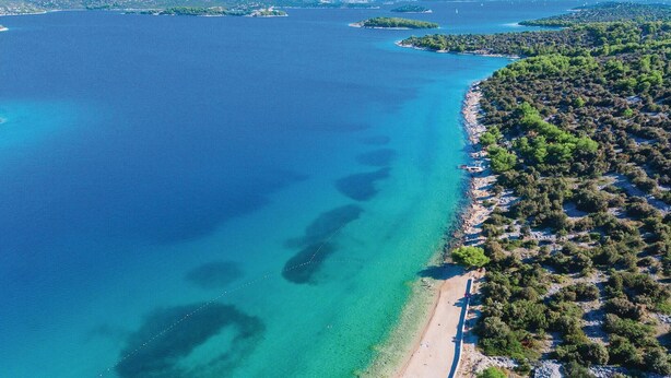 Vista aérea de una zona costera con aguas azules cristalinas, una playa de arena y abundante vegetación.