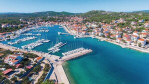 Vista aérea de un pueblo costero con un puerto deportivo, casas con techos rojos y aguas azules cristalinas.