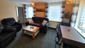 Een woonkamer met een bank, fauteuil, salontafel en een eettafel.