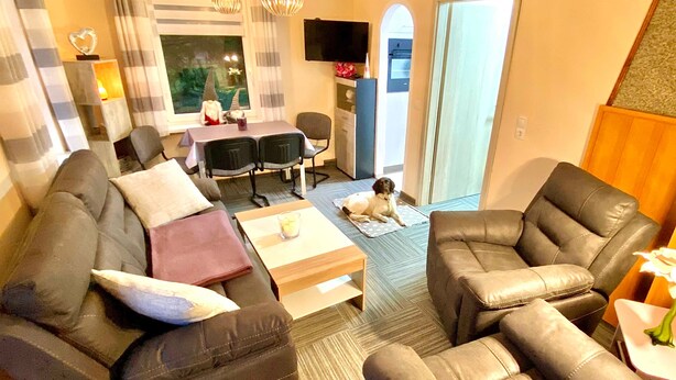 Een woonkamer met een bank, fauteuils, een salontafel en een hond op een vloerkleed.