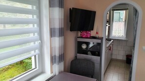 Een kamer met een tafel, een stoel, een televisie, een raam met jaloezieën, een gordijn en een klein tafeltje met een kaars.