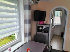 A room with a table, a chair, a TV, a window with blinds, a curtain, and a small table with a candle. - Holiday house Harz dream (Sorge)