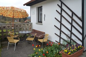 A patio with a table and chairs, a wooden bench, a climbing wall, and a flower bed with tulips.