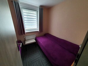 A small room with a single bed, a radiator, a window with curtains, and a door.