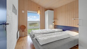 Een moderne slaapkamer met twee bedden, houten wanden, een groot raam en een hanglamp.