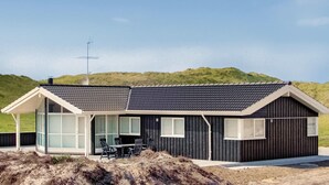 Une maison de plage moderne dotée d’une grande porte-fenêtre, d’un patio avec mobilier d’extérieur et d’un toit en pente.