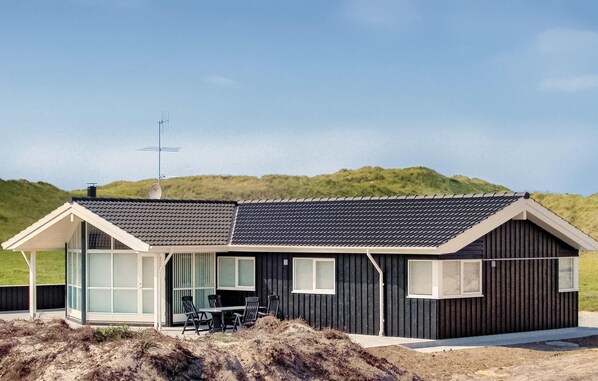 Een modern strandhuis met een ruime glazen voordeur, een terras met tuinmeubilair, en een schuin dak.