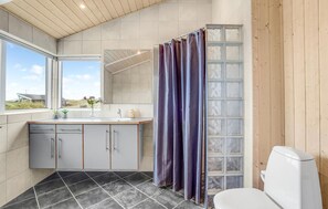 Een moderne badkamer met douchegordijn, toilet, wastafel met spiegel en kastjes.