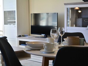 A dining area with a table set for two, a television in the background, and a cabinet with kitchenware.