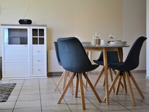 Ein Essbereich mit einem weißen Schrank, zwei dunklen Stühlen, einem Holztisch und einer Heizung.