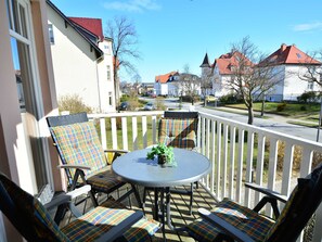 En balkong med ett runt bord och stolar, en liten växt och utsikt över en bostadsgata med hus.