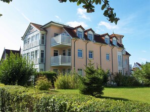 Ett hotell med flera våningar, balkonger, en trädgård och en klar himmel.